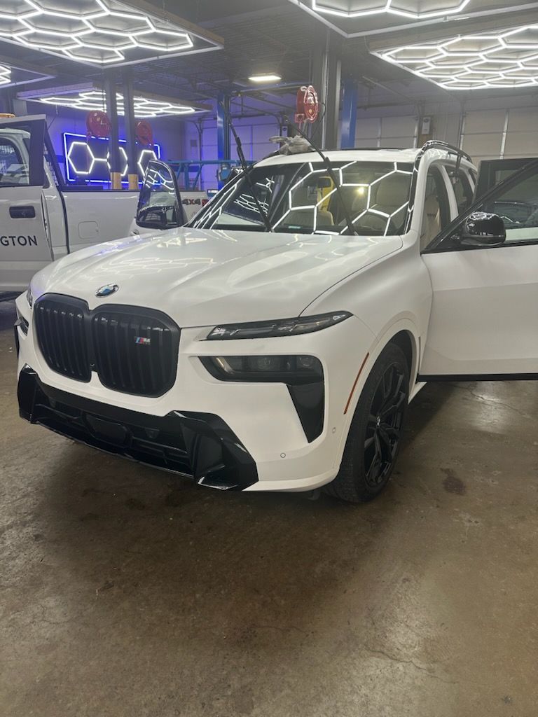 White BMW X7 SUV with black accents, parked indoors with open doors.