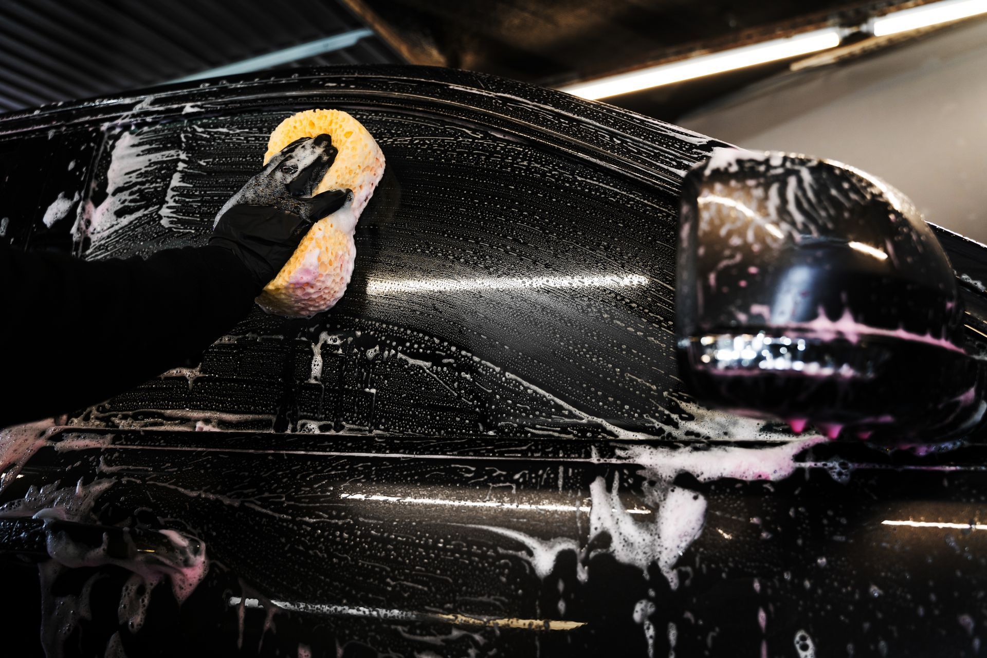 Person washing a black car with a sponge and soapy water.