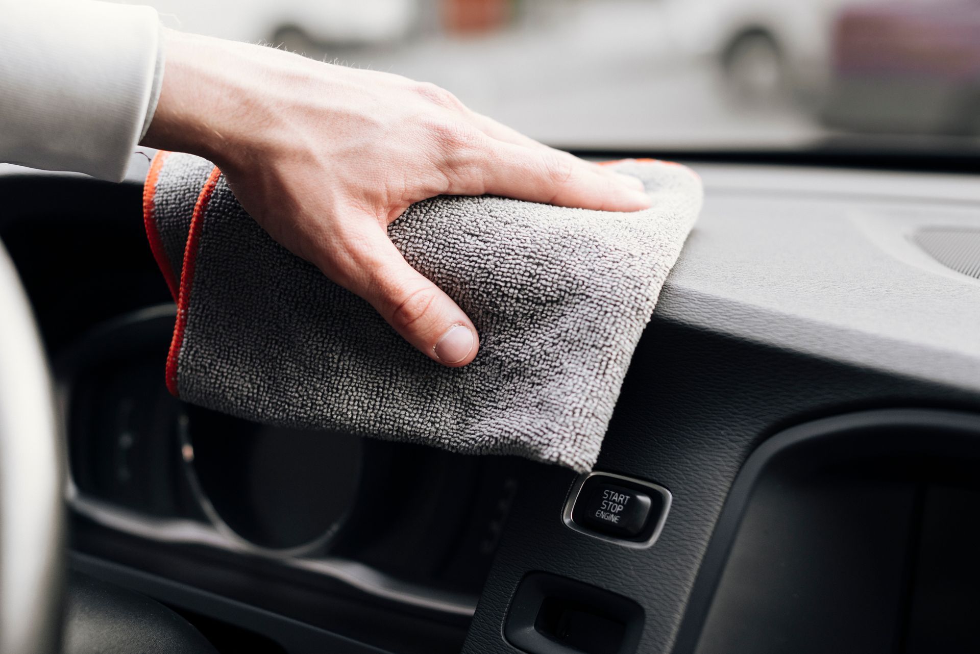 Hand wiping a gray microfiber cloth across a car dashboard.