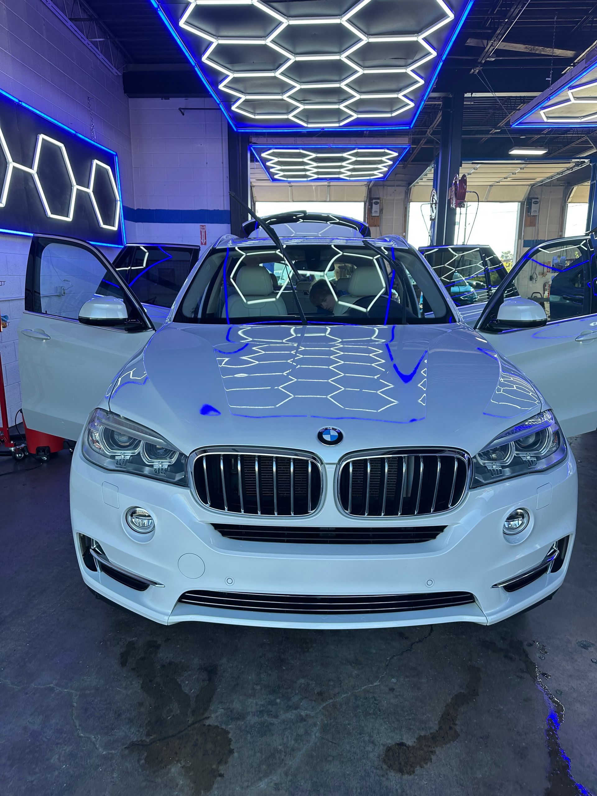 White BMW X7 M SUV with black accents in a car wash bay.