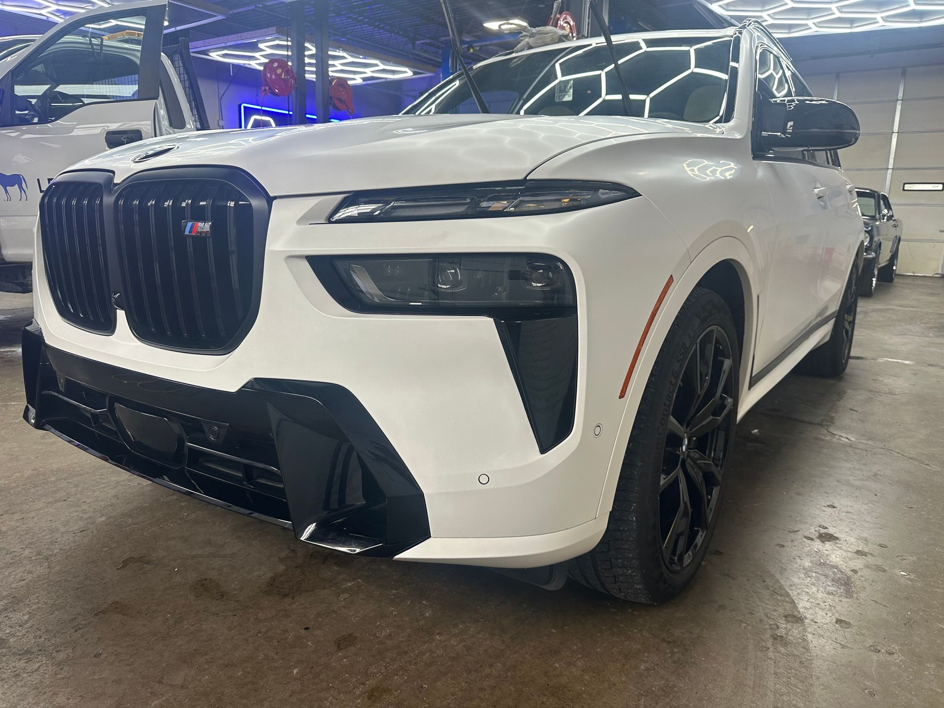 White BMW X7 M SUV with black accents in a car wash bay.