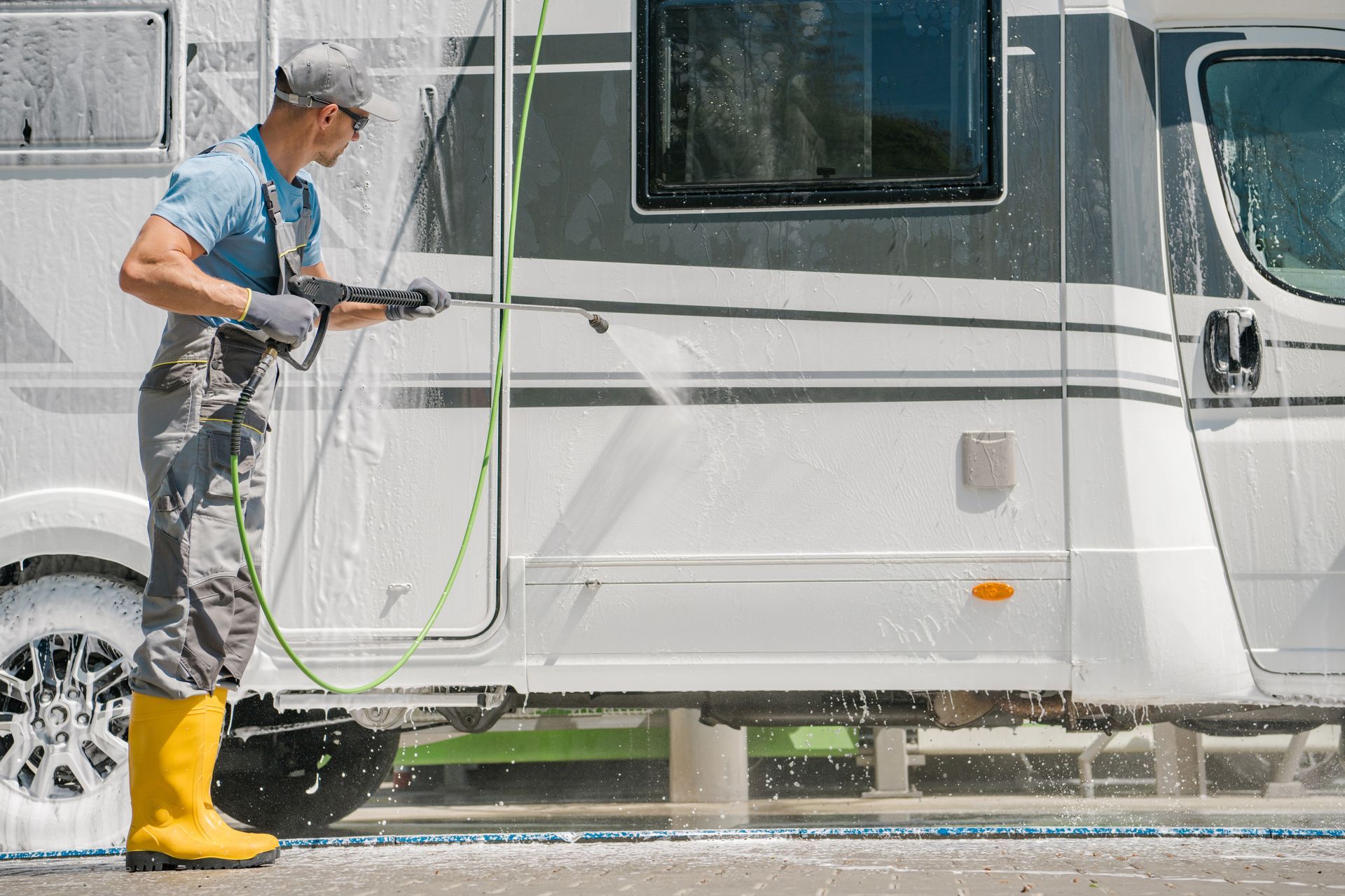 Man power washing a white and gray RV with soapy water.