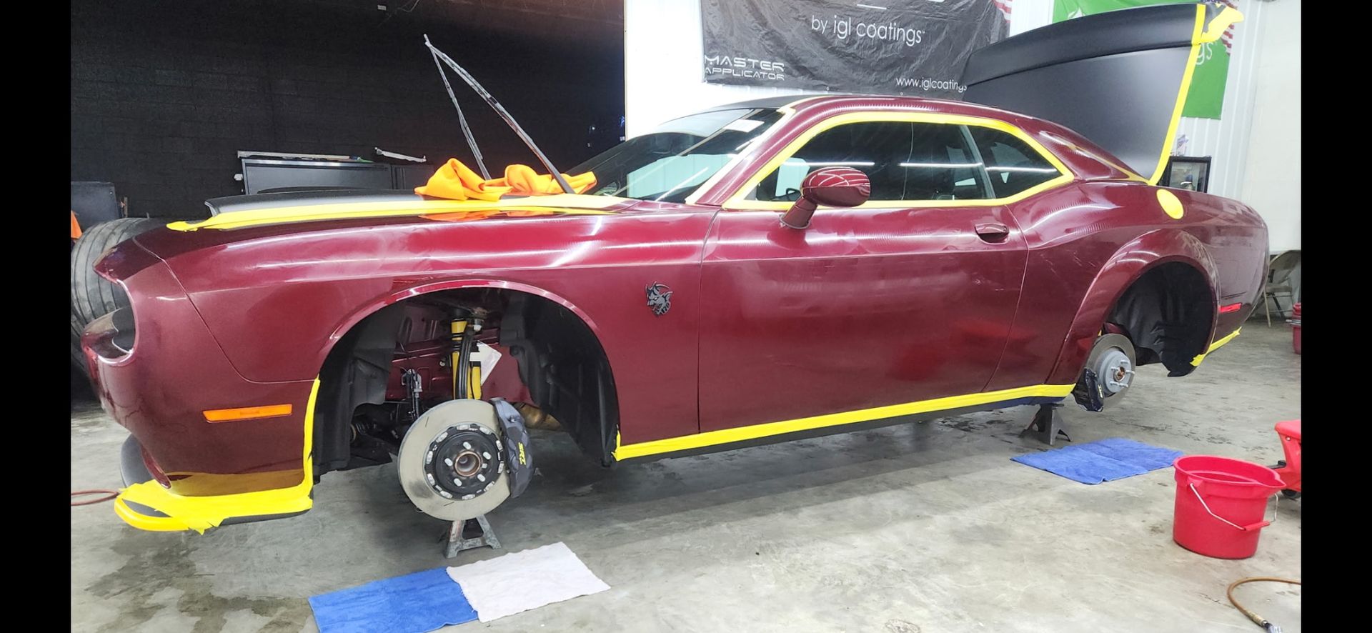 A maroon Dodge Challenger being worked on in a garage with yellow tape and the hood open.