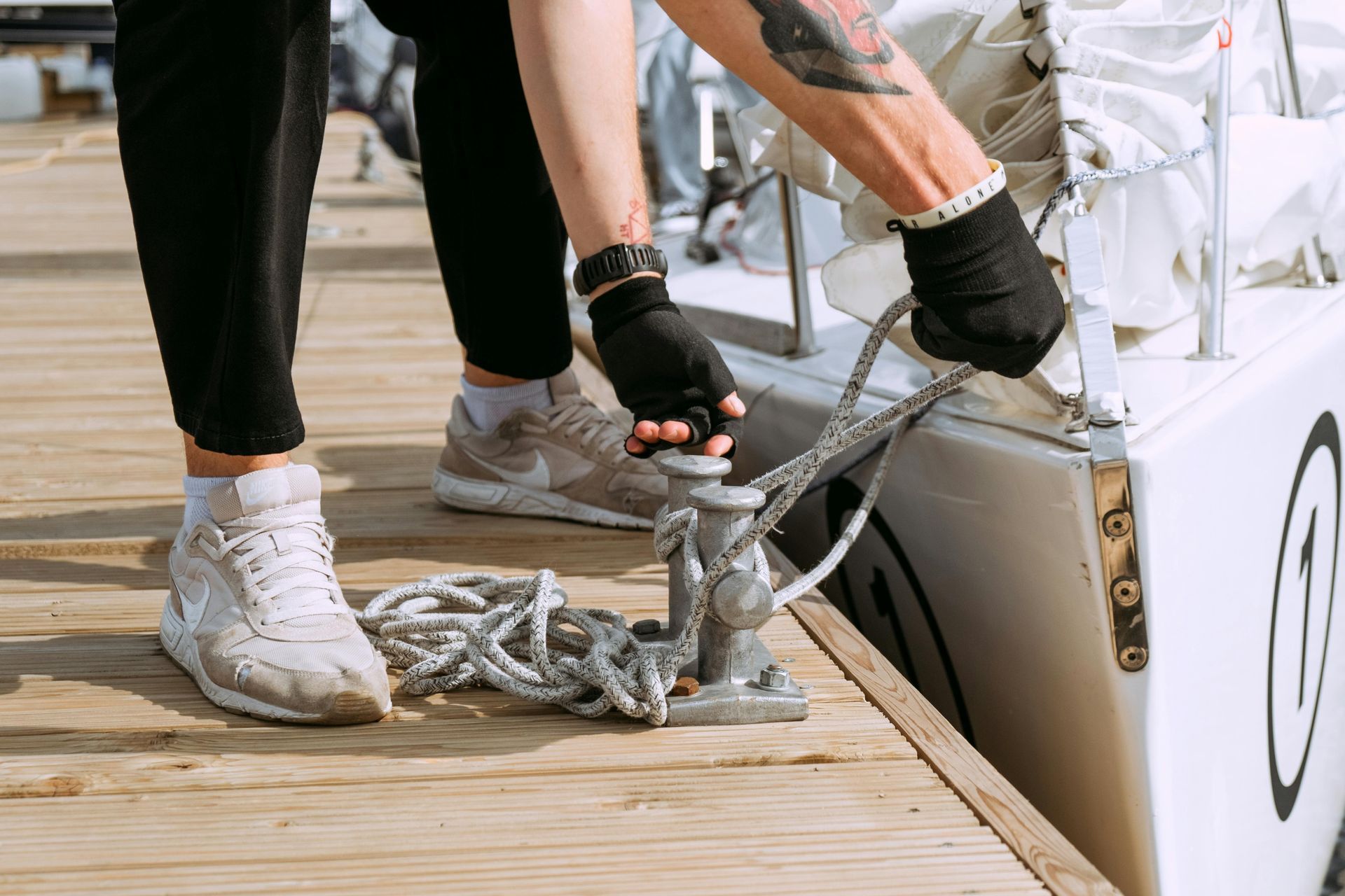 Person tying boat to dock with rope, wearing black gloves and sneakers.
