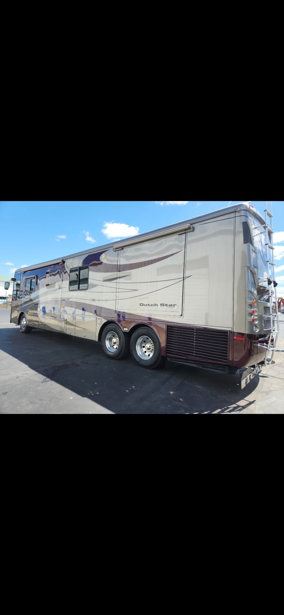 Large beige and brown RV parked on asphalt on a sunny day.