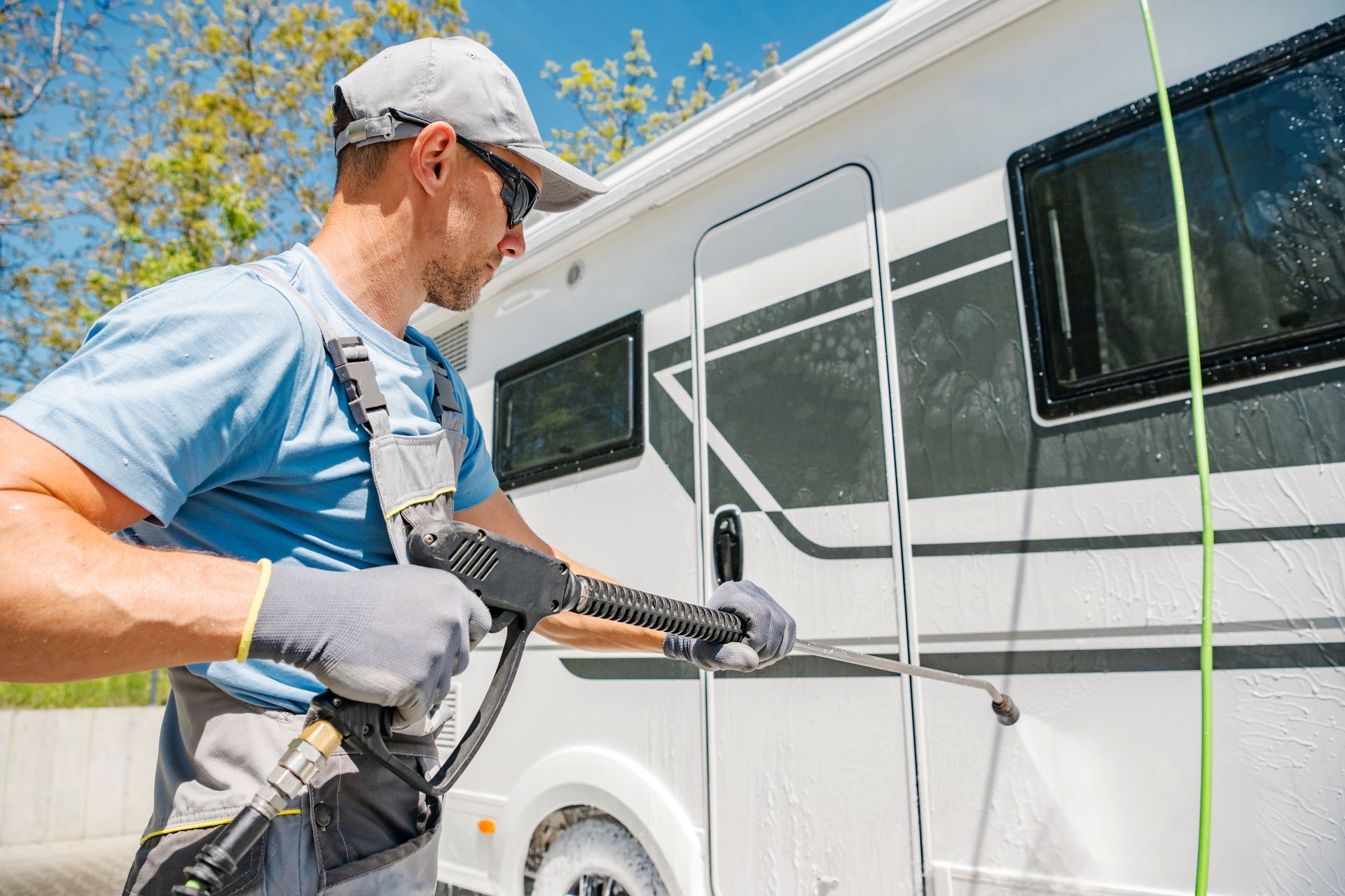 Man power washing a white camper van on a sunny day.