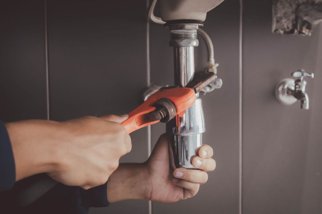 Idraulico che usa una chiave inglese su un tubo del lavandino in un bagno.