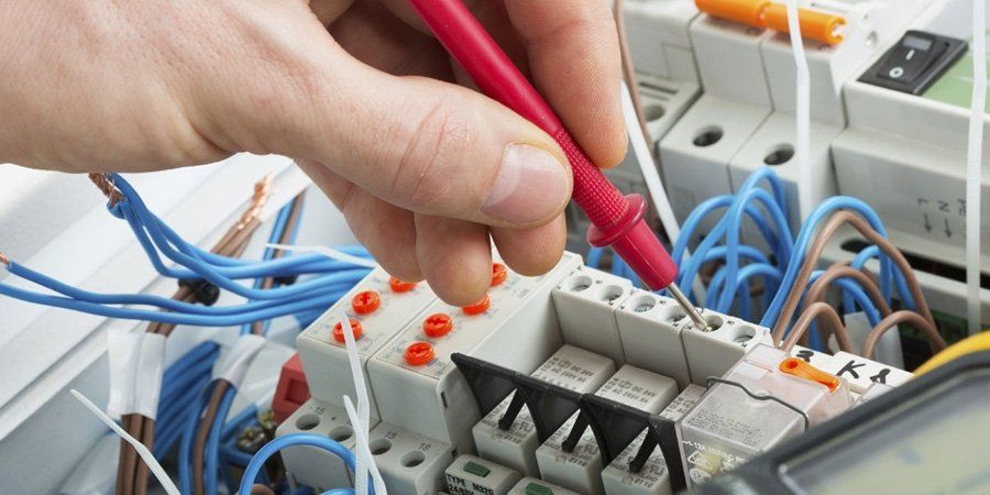 Una mano che usa una sonda rossa del multimetro per testare un circuito stampato con fili blu e marroni.