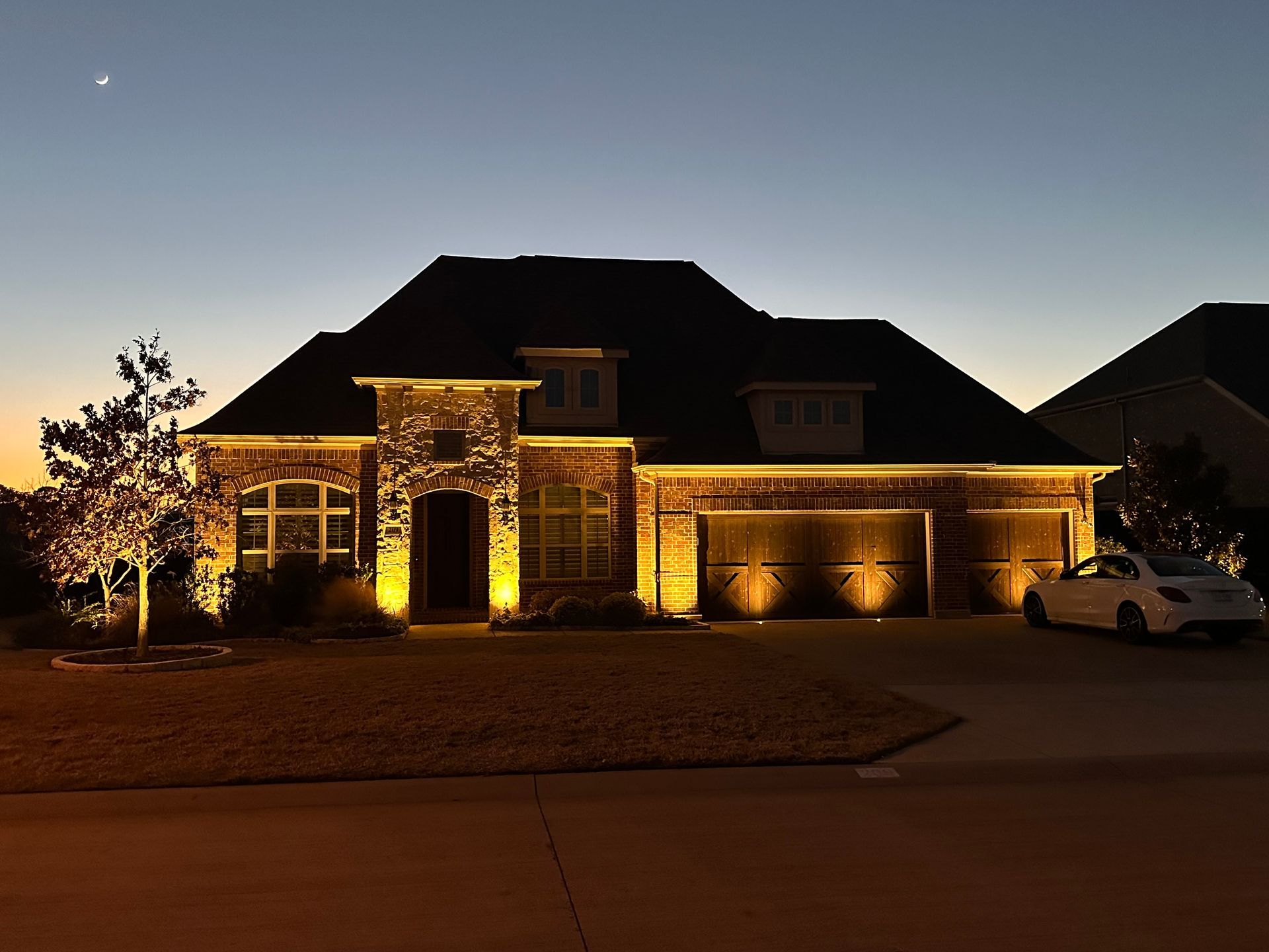 A house is lit up at night with a car parked in front of it.