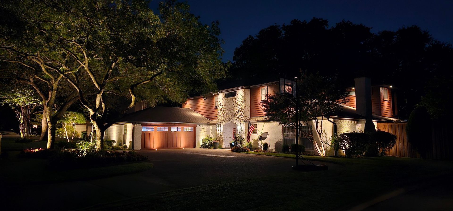 A large house is lit up at night with trees in front of it.