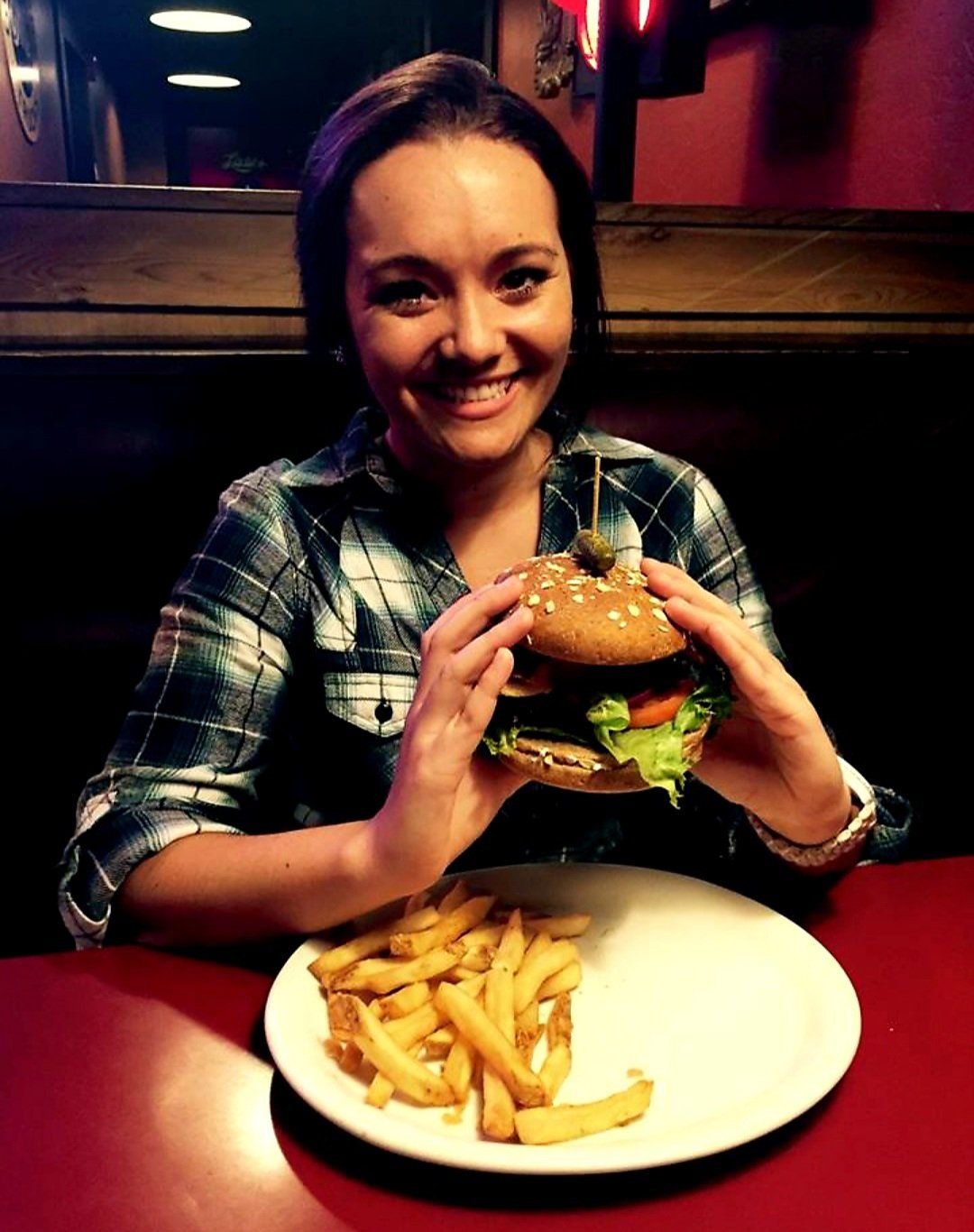 A woman holding a hamburger next to a plate of french fries