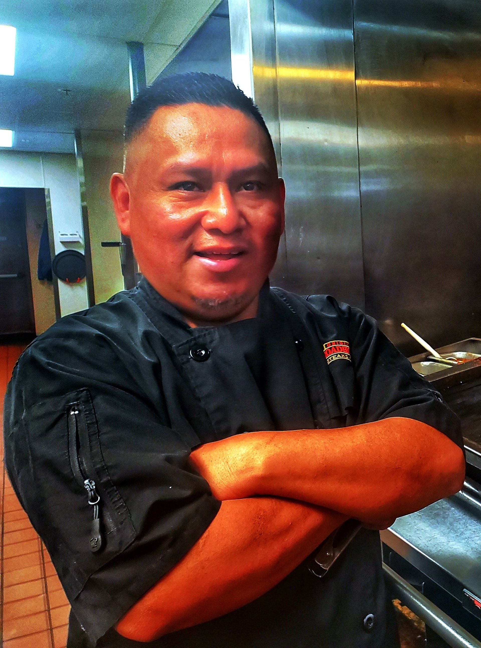A man in a chef 's uniform has his arms crossed