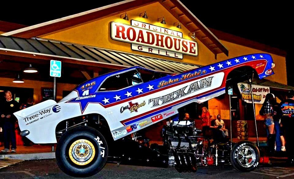 A red white and blue muscle car is parked in front of a roadhouse restaurant