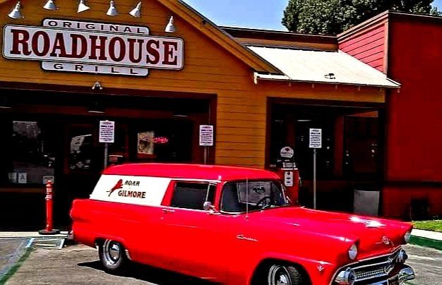 A red car is parked in front of a building that says roadhouse