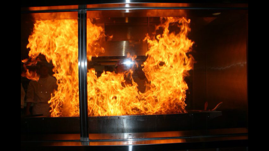 A large fire is coming out of a stainless steel oven.