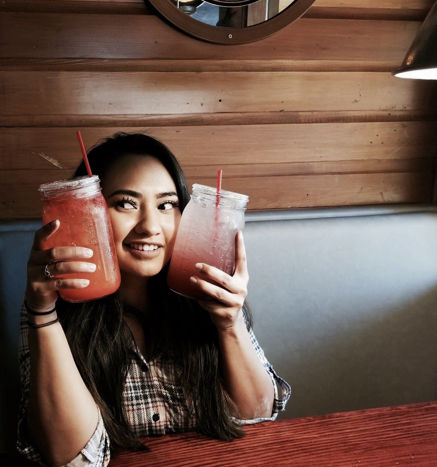 A woman is sitting at a table holding two drinks