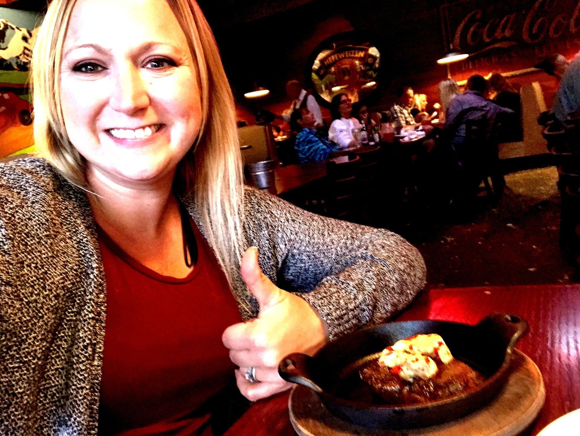 A woman is giving a thumbs up in front of a coca cola sign