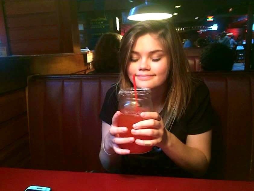 A girl is drinking from a mason jar with a straw