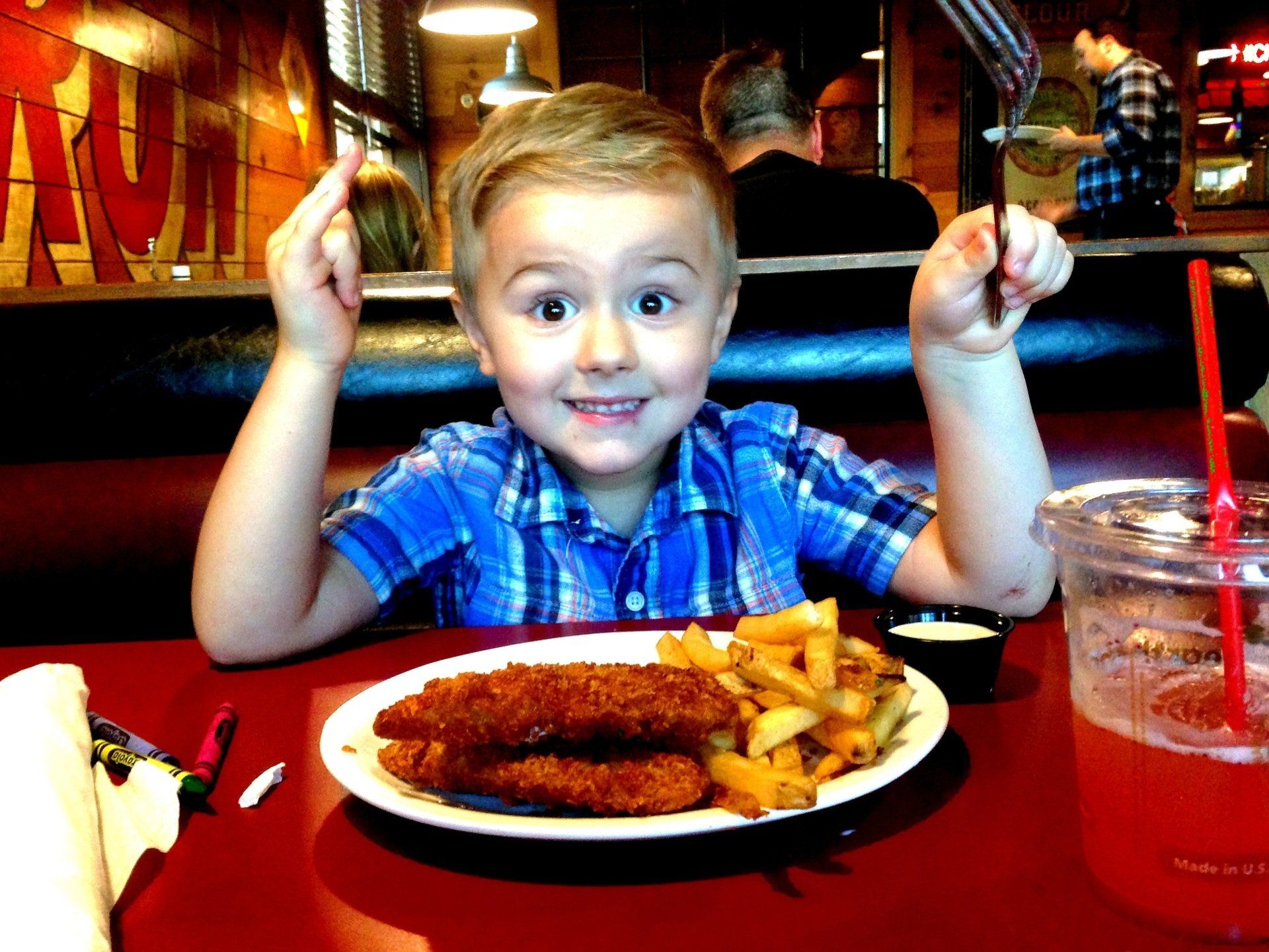 A little boy is sitting at a table with a plate of food and a drink