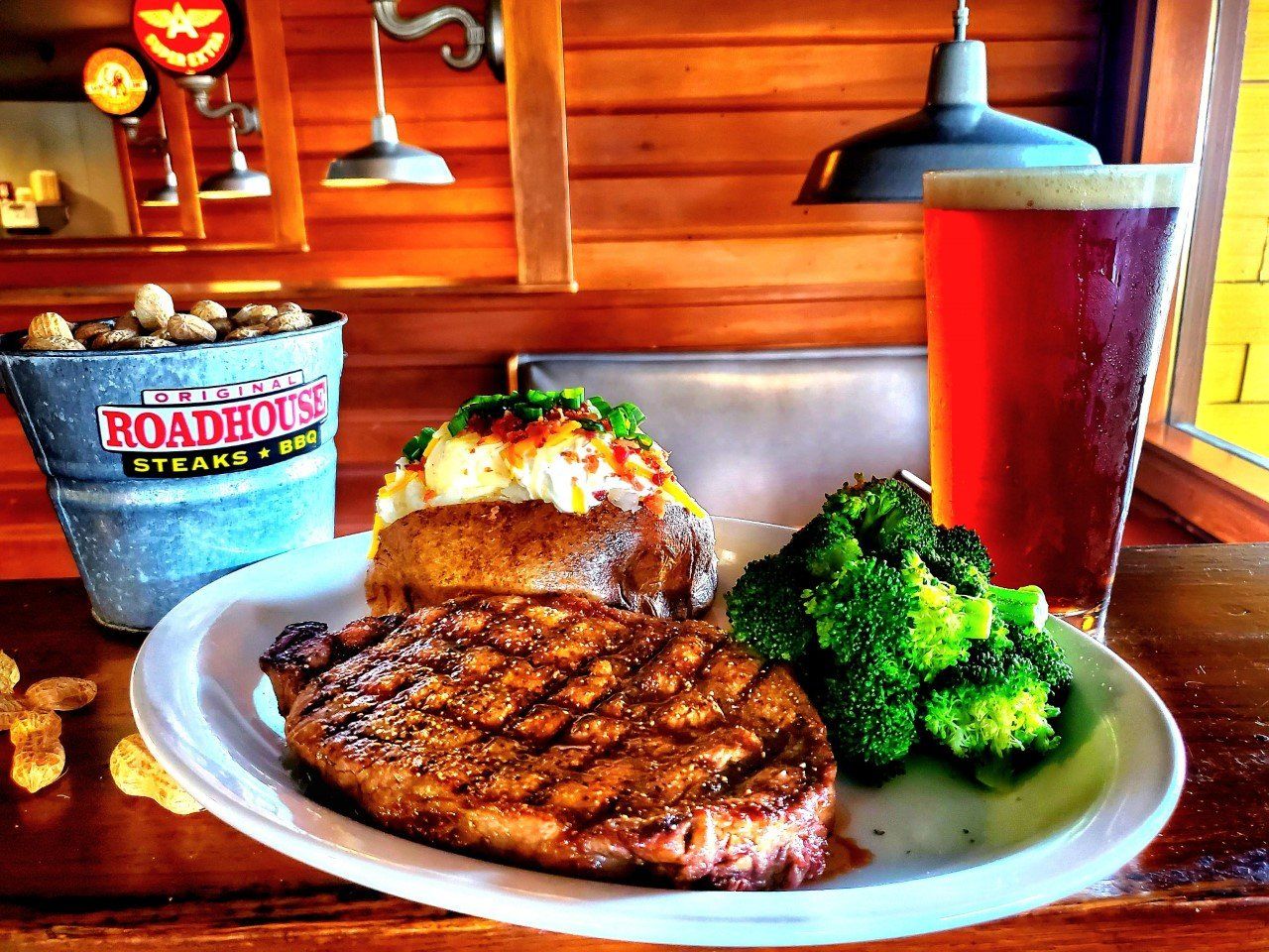 A steak and broccoli on a plate next to a glass of beer