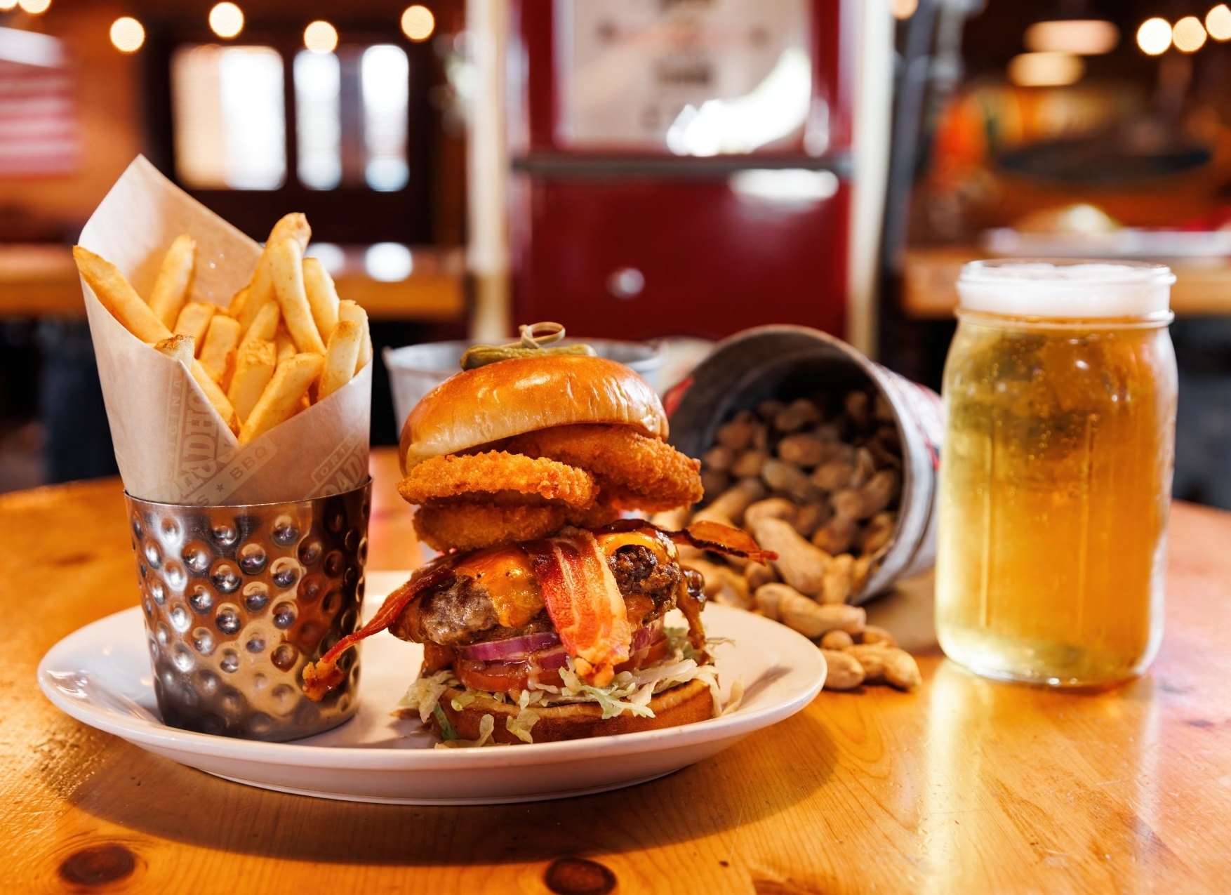 A plate of food with a hamburger , french fries and a glass of beer on a table.