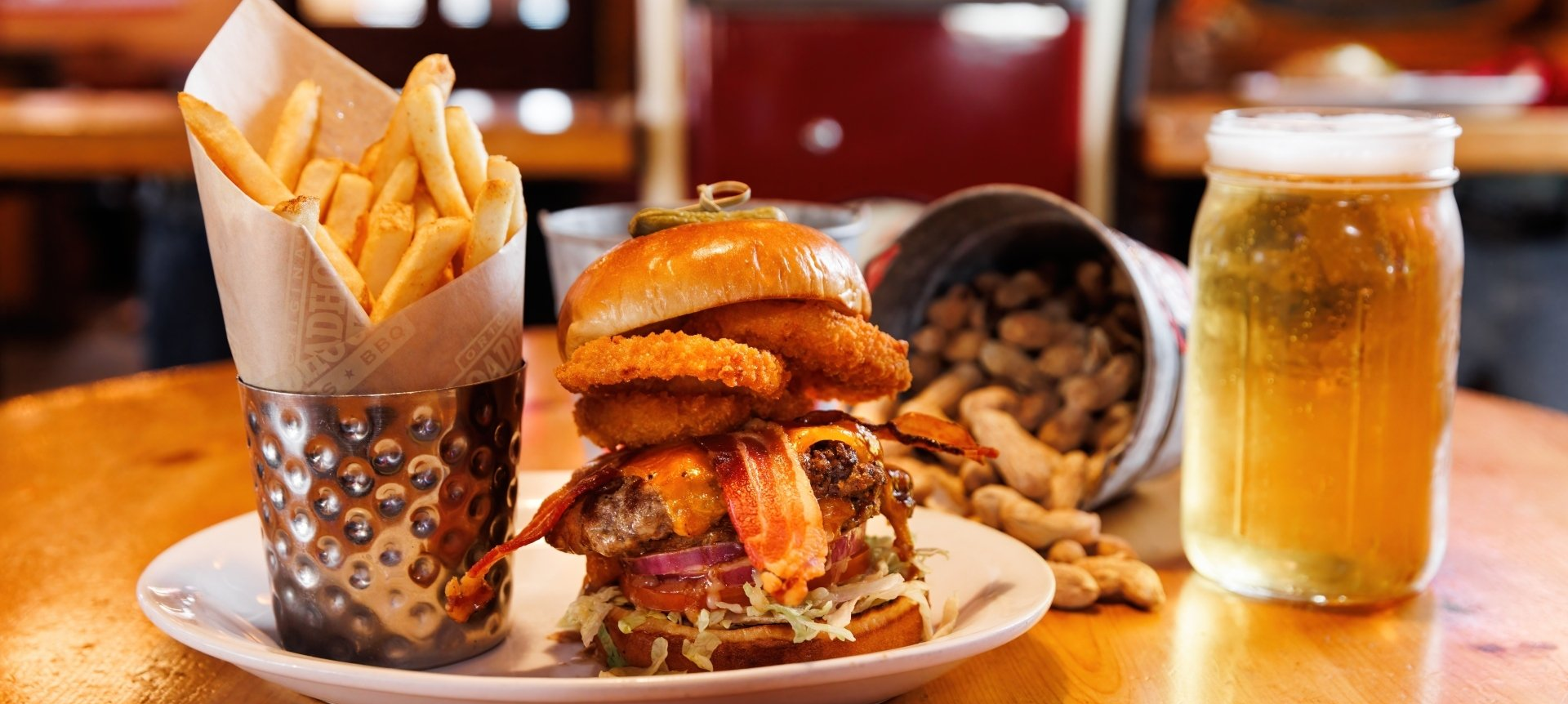 A hamburger , french fries , peanuts and a glass of beer on a table.