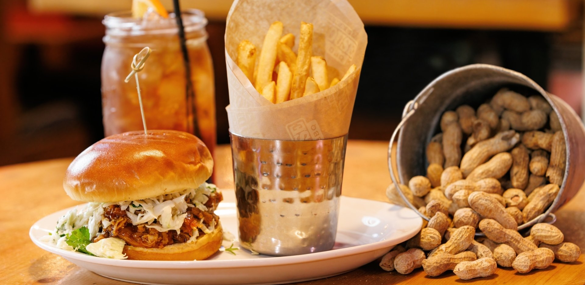 A plate of food with a hamburger , french fries and peanuts on a table.