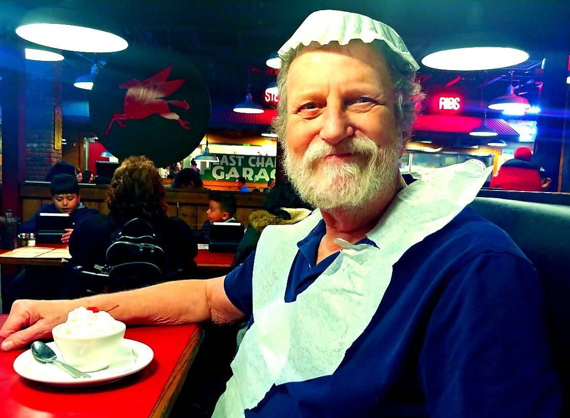 A man wearing an apron sits at a table in a restaurant