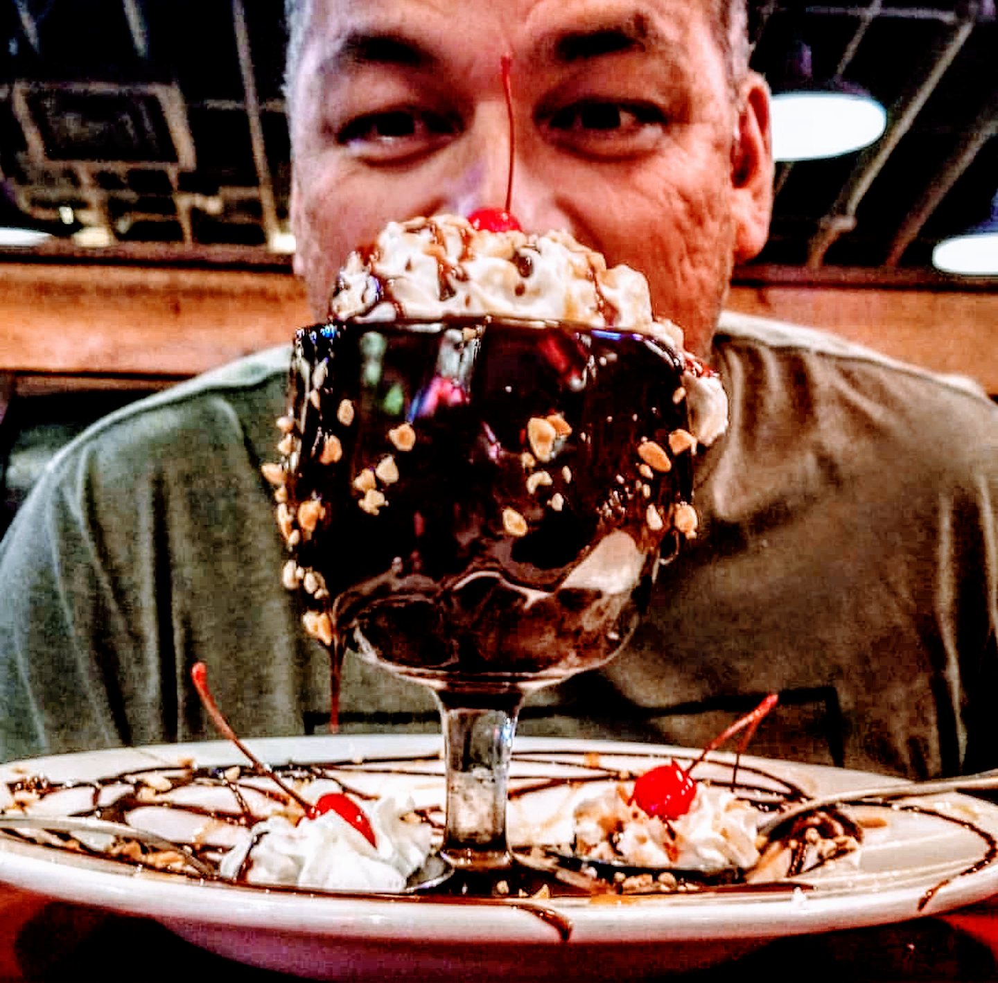 A man is eating a chocolate sundae with whipped cream and a cherry on top.