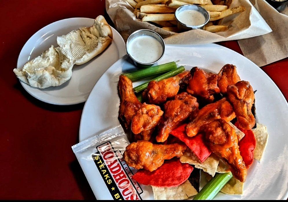 A white plate topped with chicken wings next to a bag of madhouse steak sauce