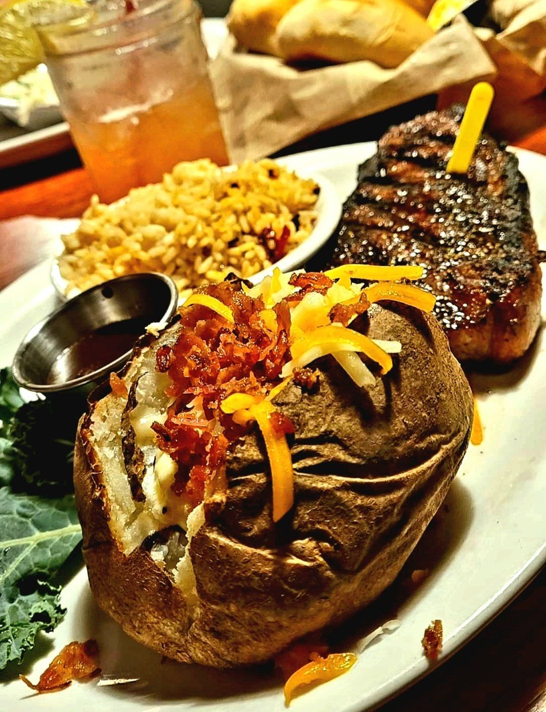 A baked potato stuffed with cheese and bacon next to a steak on a plate