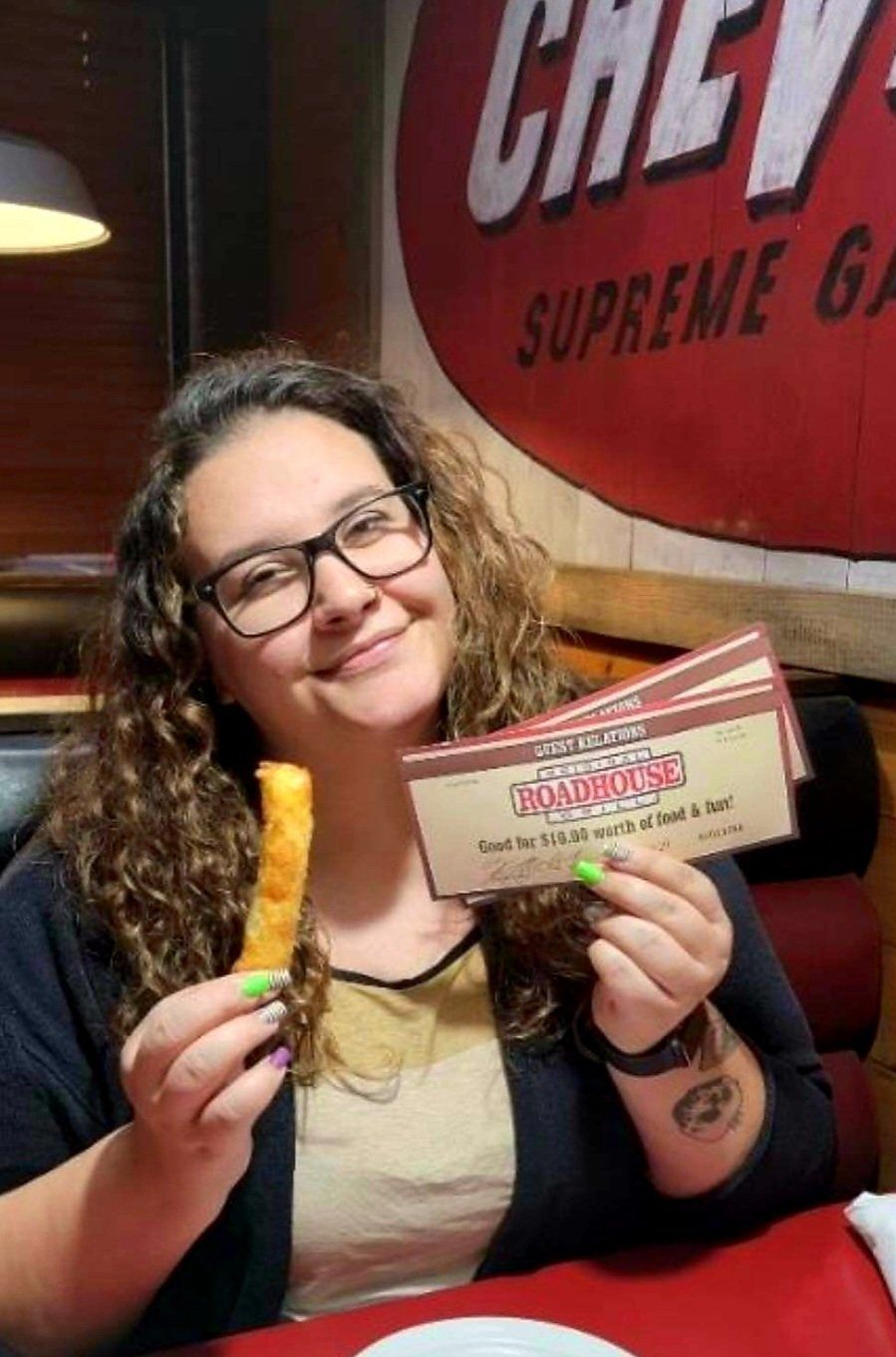 A woman is sitting at a table holding a piece of food and a chevy sign in the background
