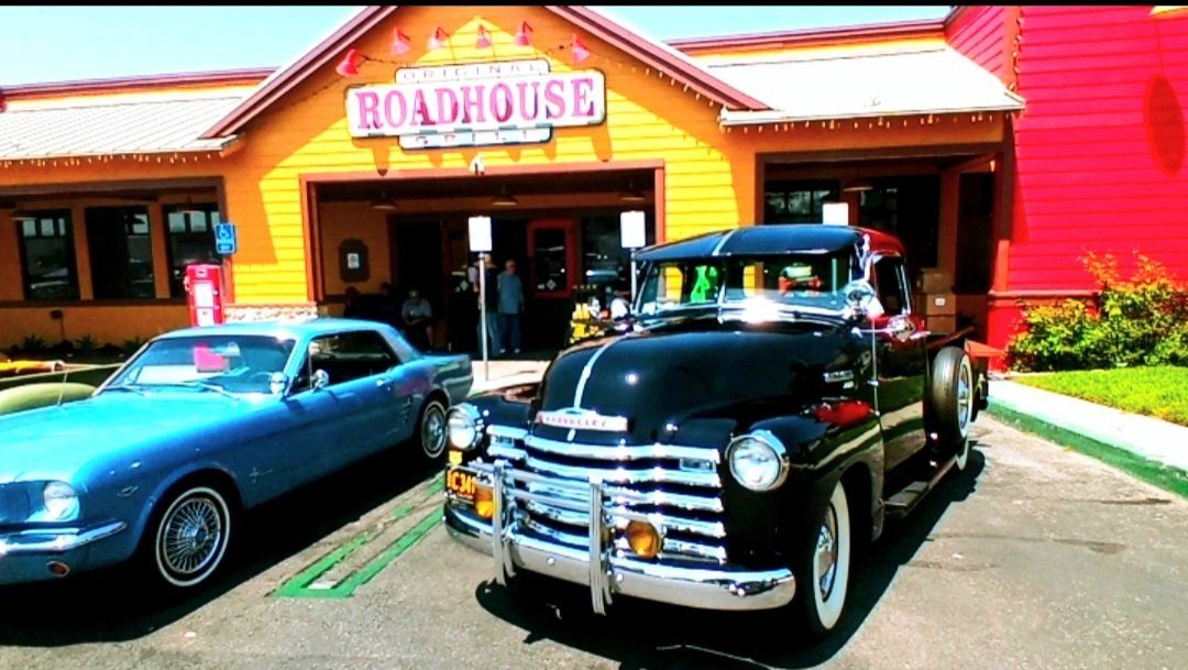 Two old cars are parked in front of a building that says roadhouse