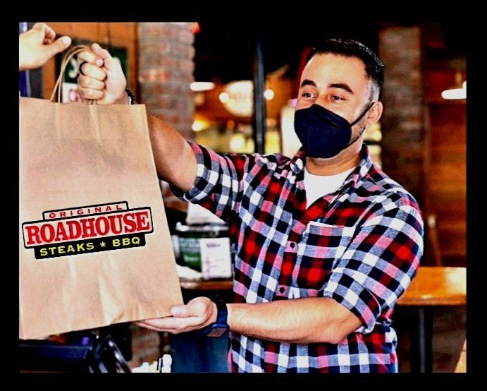 A man wearing a mask is holding a bag that says roadhouse steaks bbq