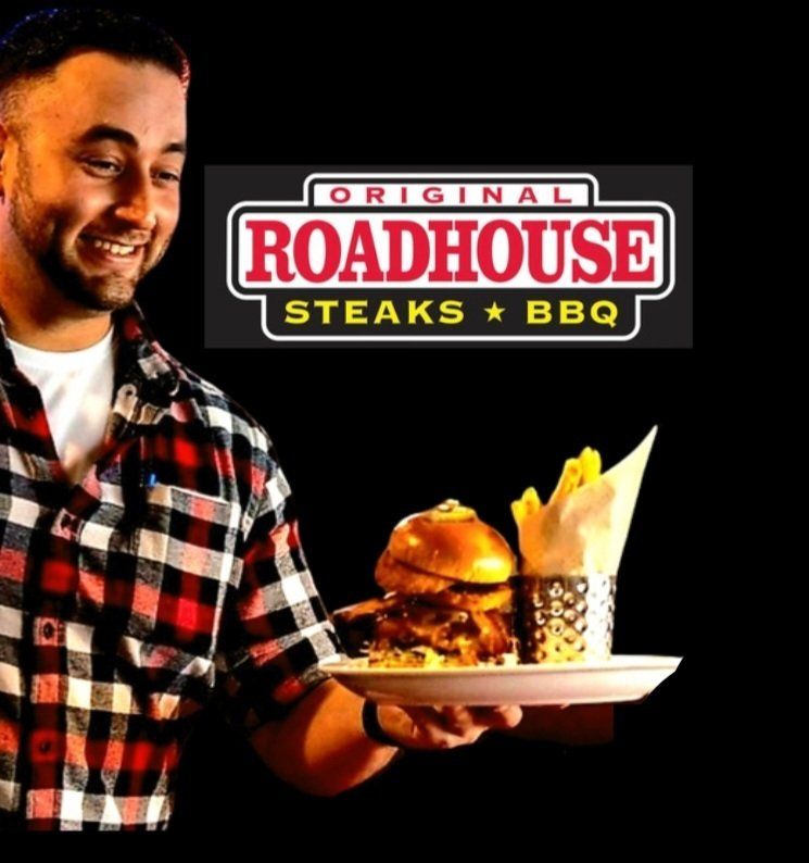 A man is holding a plate of food in front of a sign for roadhouse steaks bbq