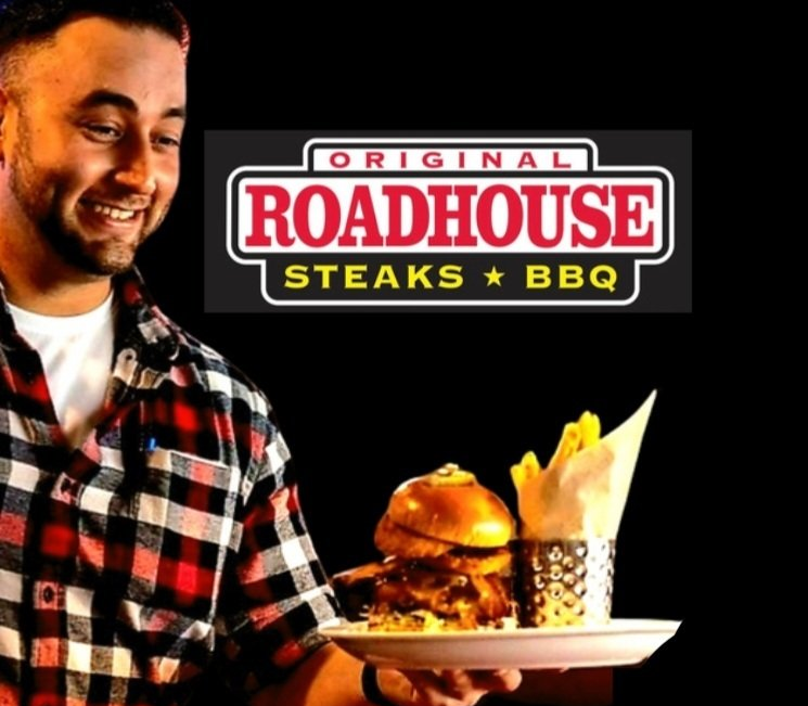 A man holding a plate of food in front of a sign for roadhouse steaks bbq