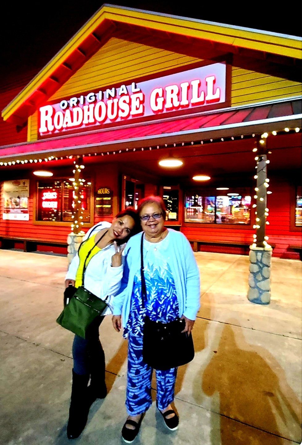 Two women are posing for a picture in front of the roadhouse grill