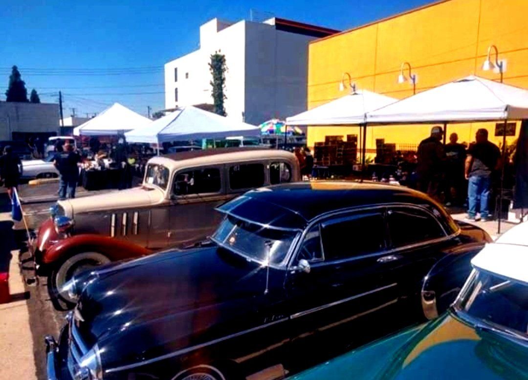 Three old cars are parked in front of a yellow building