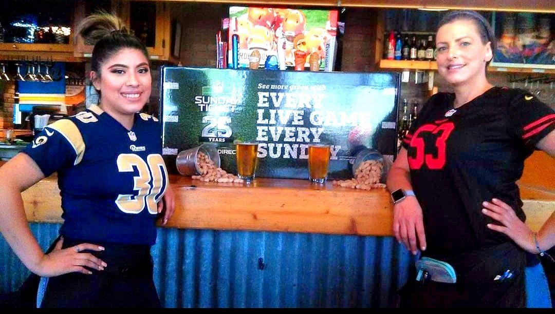 Two women are standing next to each other in front of a bar.