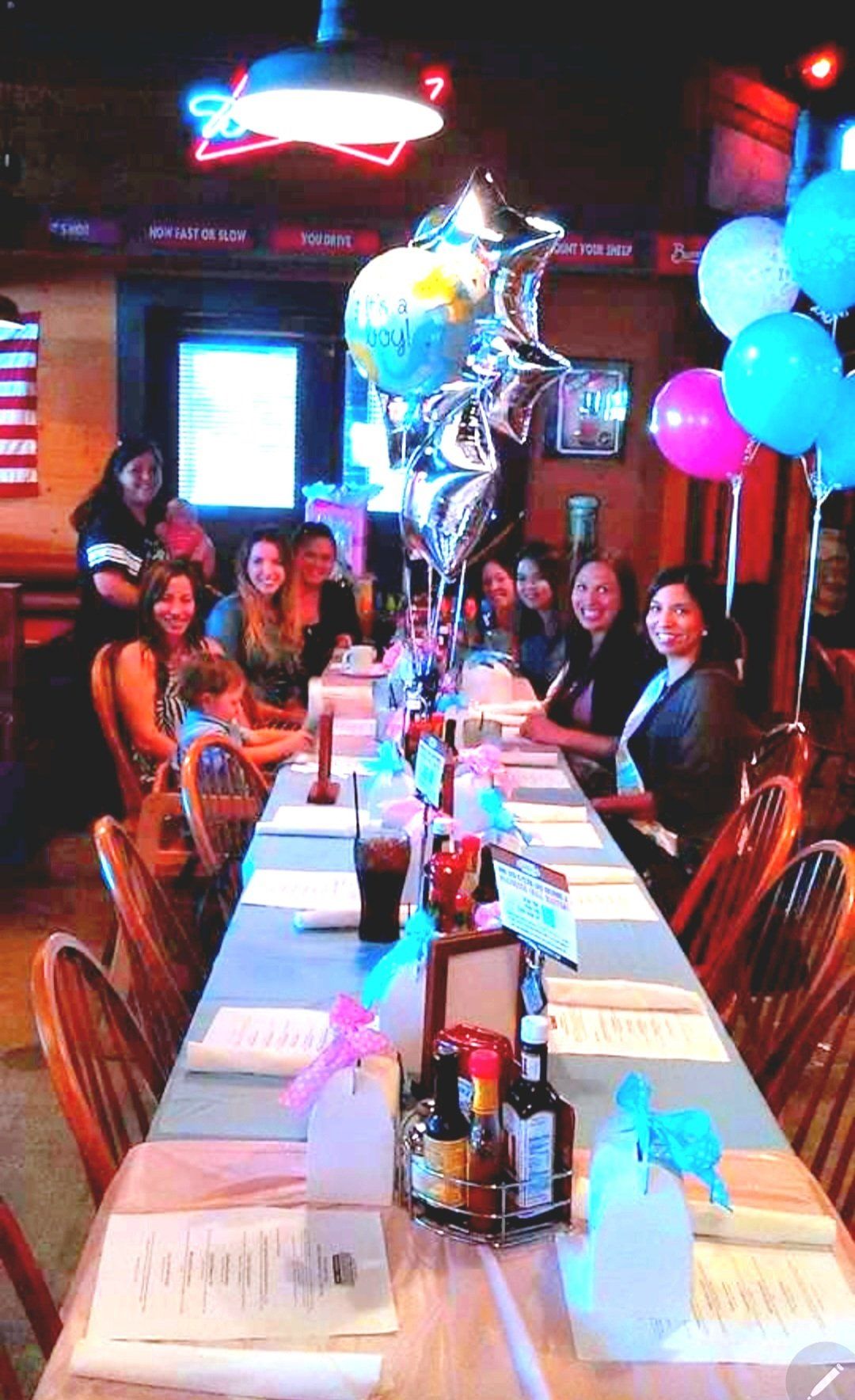A group of people are sitting at a long table with balloons on it.