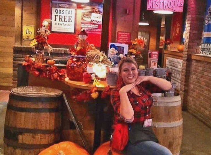 A woman sits on a barrel in front of a sign that says kids eat free