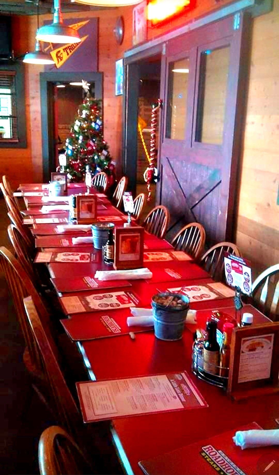 A long row of tables in a restaurant with a christmas tree in the background.