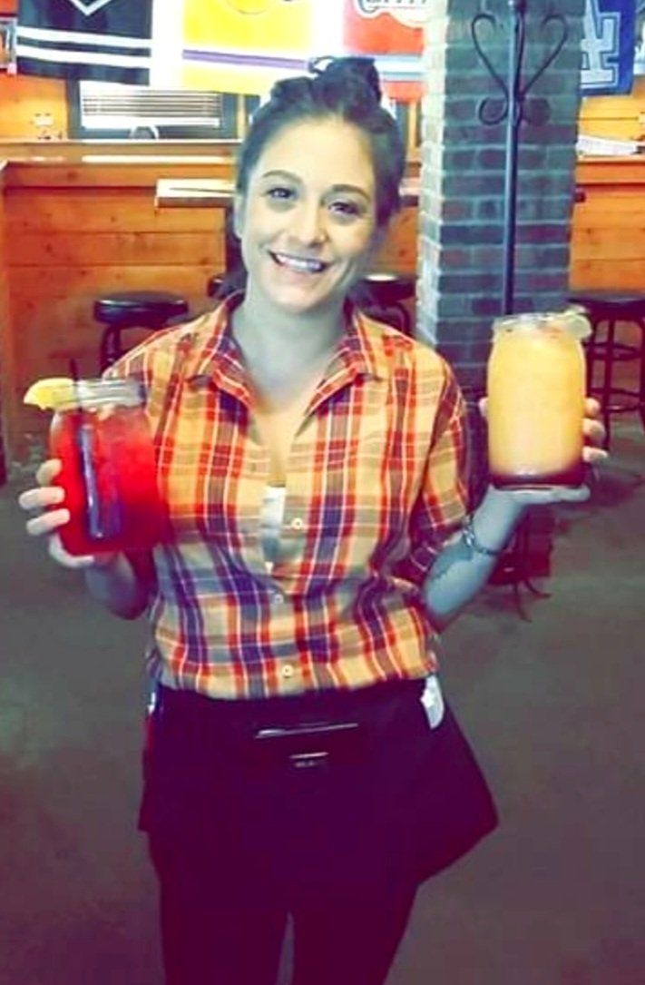A woman in a plaid shirt is holding two drinks in her hands