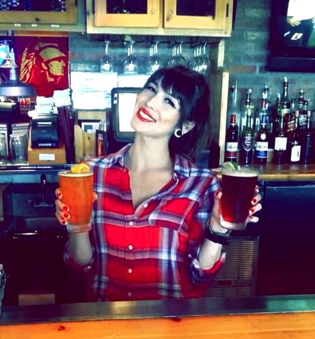 A woman in a plaid shirt is holding a drink and a beer