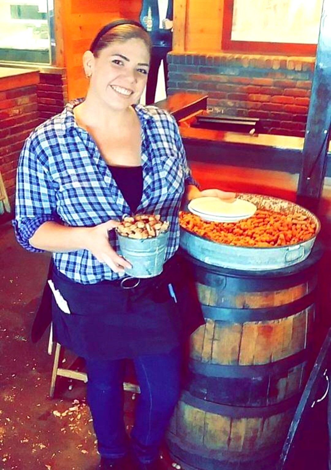 A woman is holding a bucket of food in front of a wooden barrel.