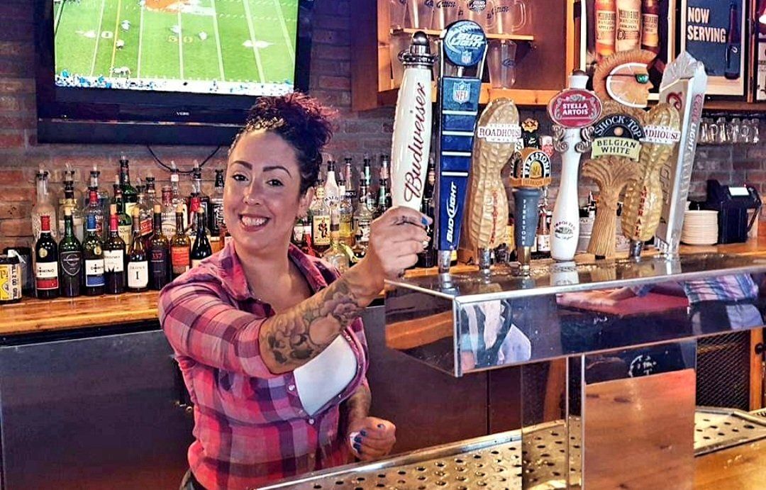 A woman is pouring beer from a tap at a bar.