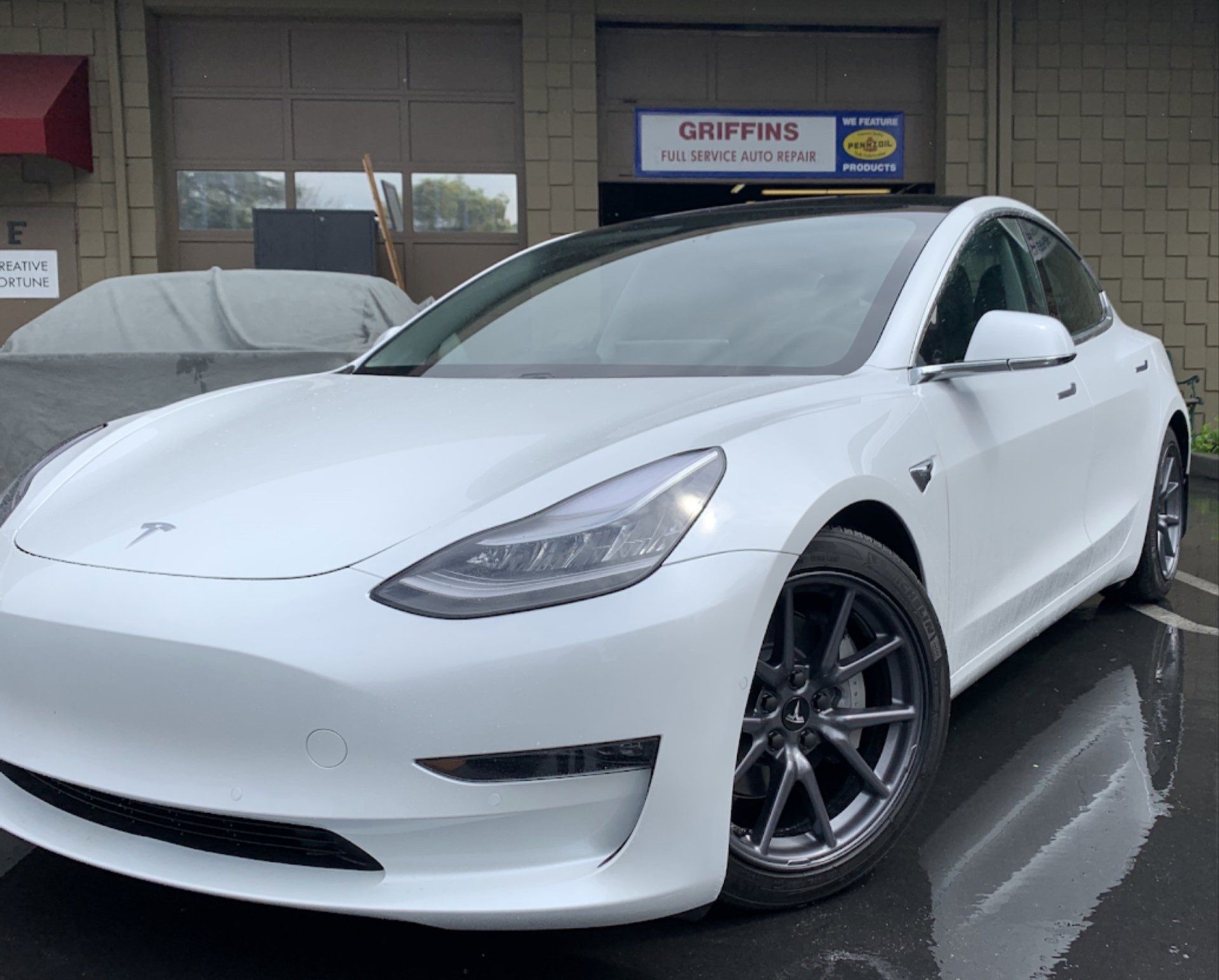 A white tesla model 3 is parked in front of a garage