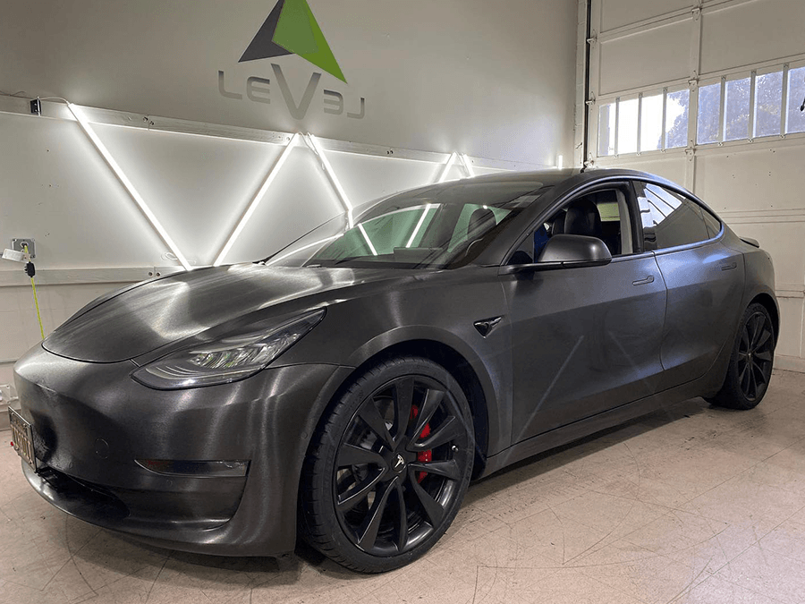 A black tesla model 3 is parked in a garage.