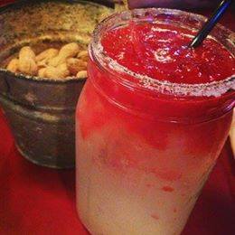 A mason jar filled with a red liquid next to a bucket of peanuts.