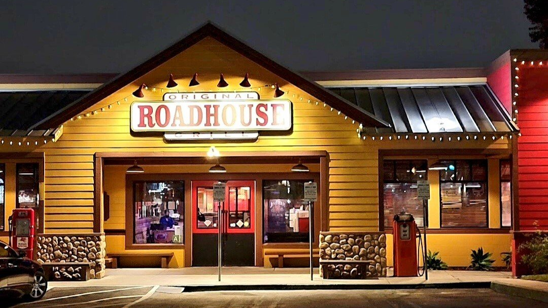 A roadhouse restaurant is lit up at night with a car parked in front of it.